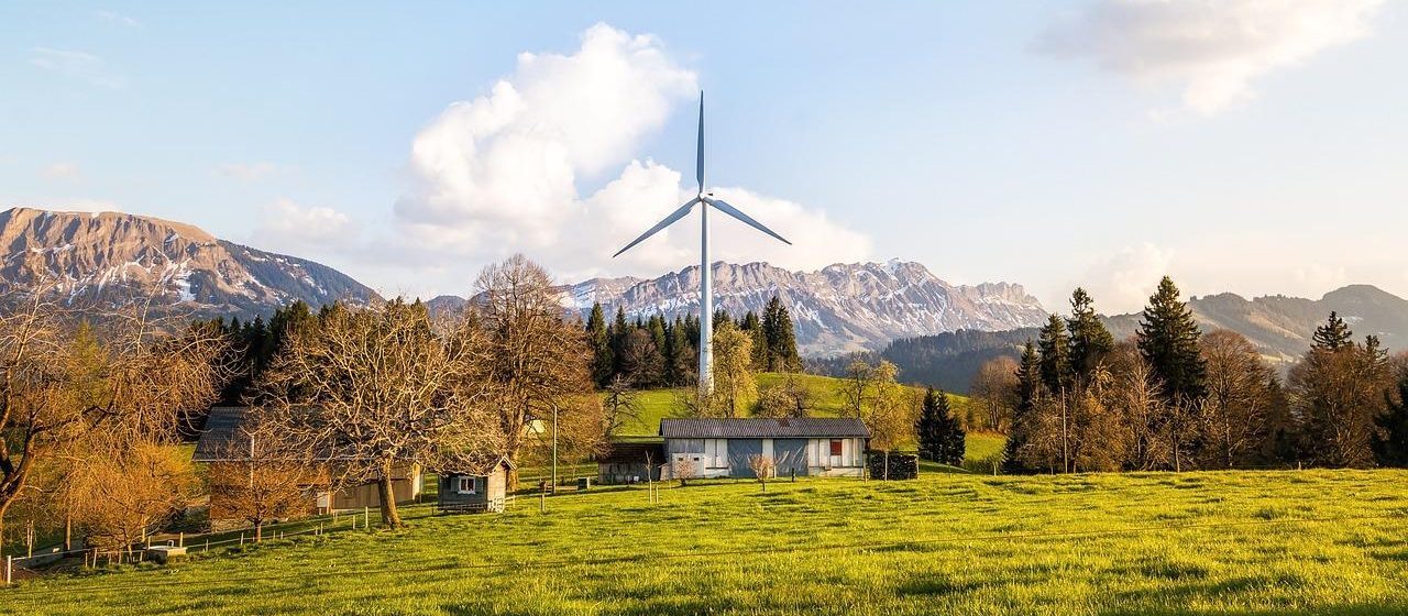 a windmill in a field with a house and mountains in the background