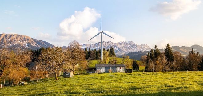 a windmill in a field with a house and mountains in the background